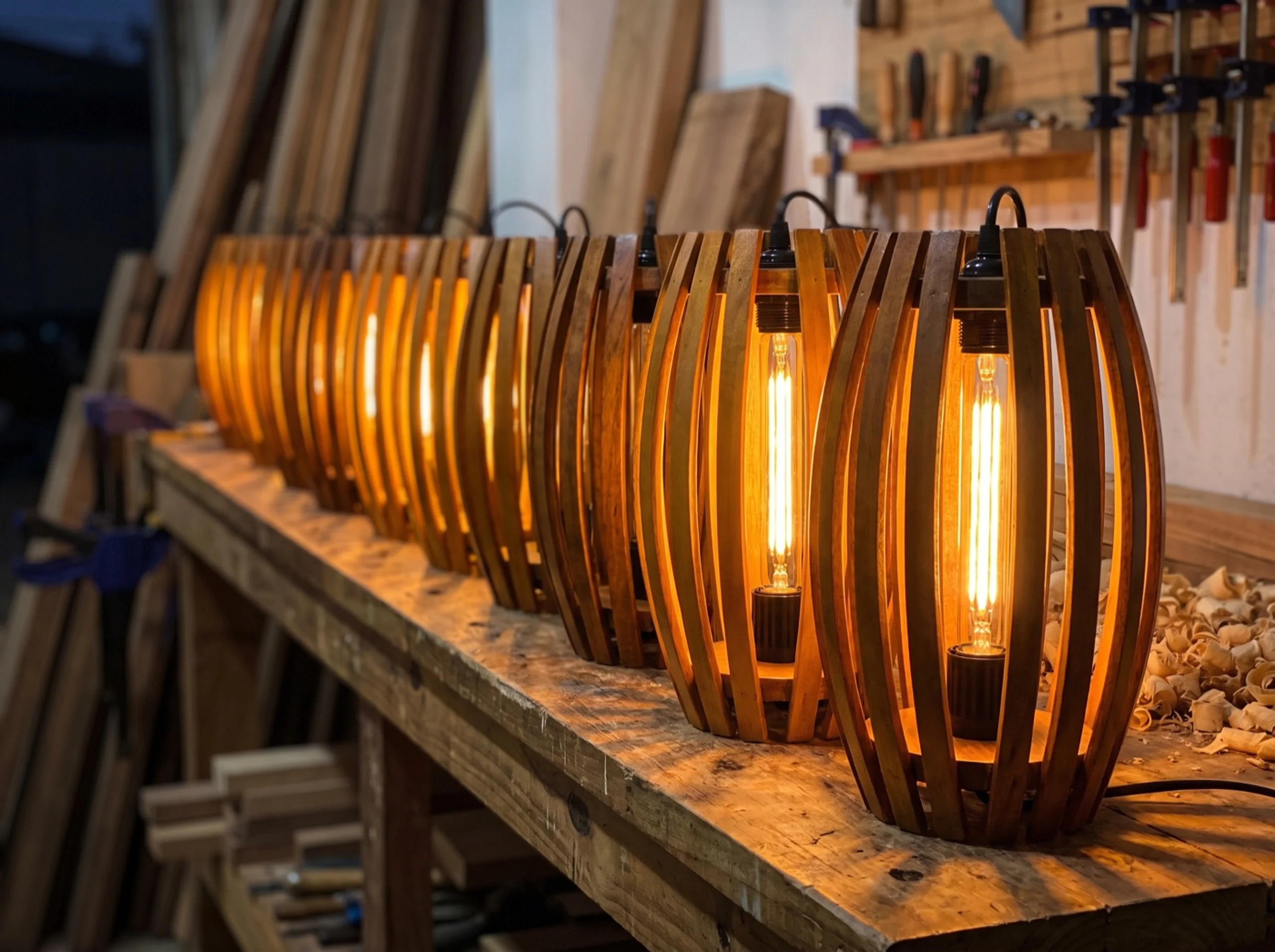 Finished wooden lanterns lined up along the workshop bench at dusk, several of them lit